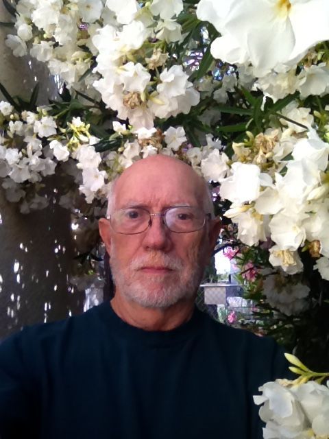 A man wearing glasses is standing in front of white flowers