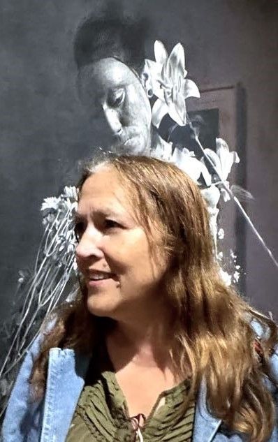 A woman is standing in front of a painting of a woman with flowers in her hair.