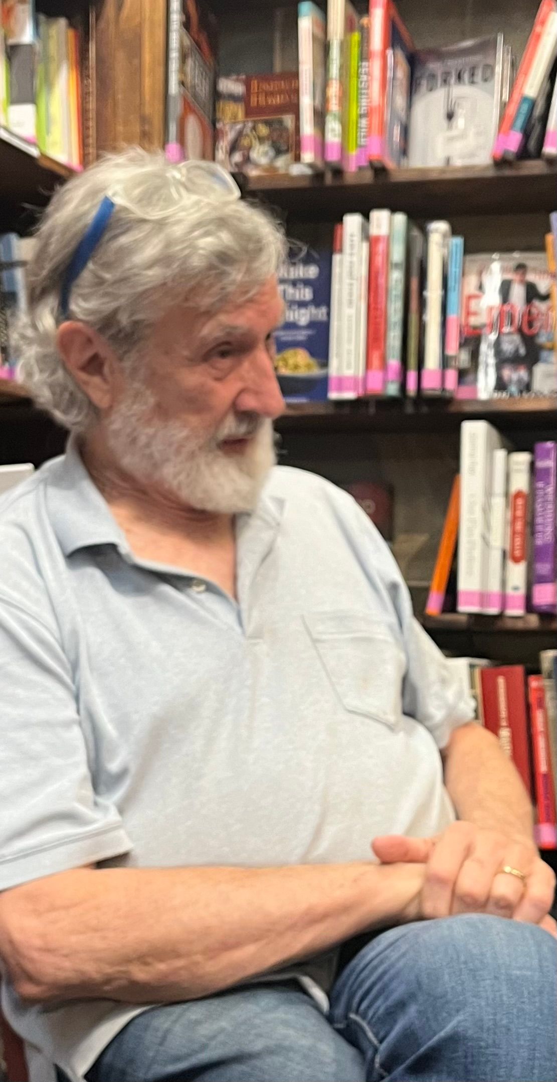 A man with a beard is sitting in front of a bookshelf in a library.