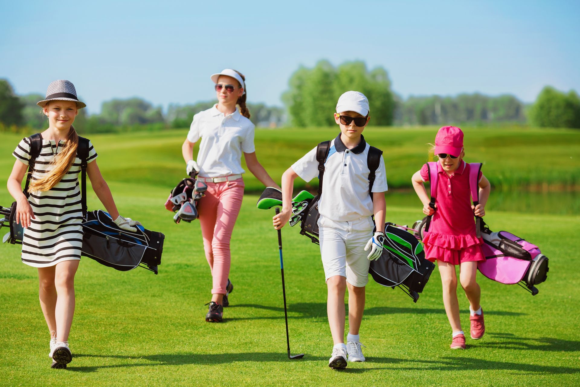 Four golfers walking across a green golf course with clubs and bags on a sunny day Four golfers walking across a green golf course with clubs and bags on a sunny day