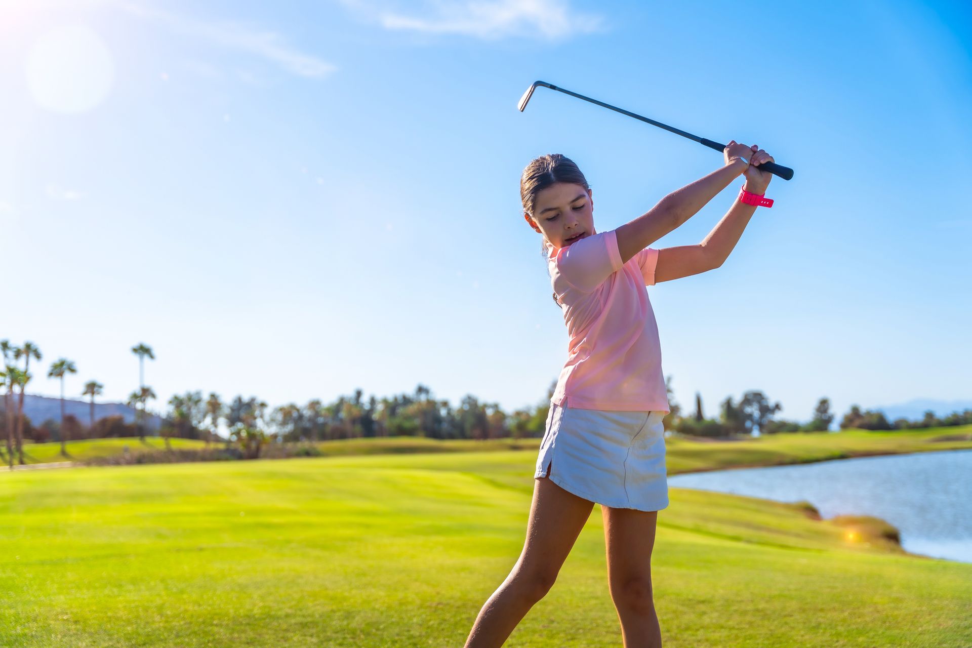 Golfer swinging a club on a sunny green course near water