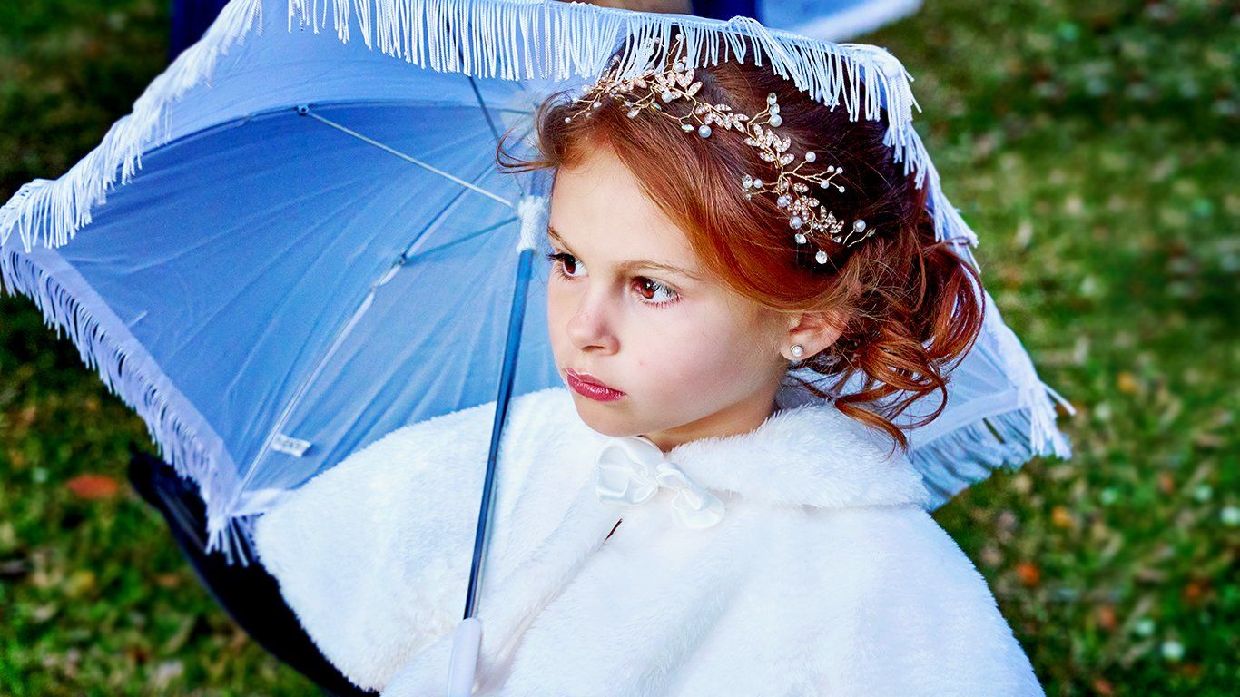 A little girl in a white coat is holding a blue umbrella.