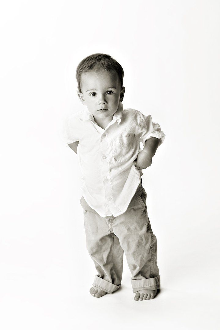 A little boy in a white shirt and khaki pants is standing on a white background.