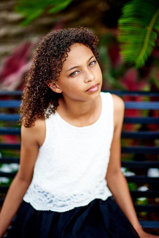 A young girl is sitting on a bench wearing a white top and a black skirt.