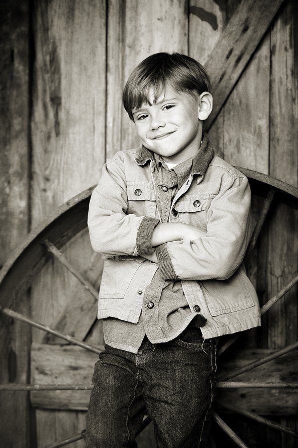 A young boy is standing in front of a wooden wall with his arms crossed.