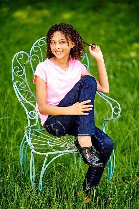 A young girl is sitting on a chair in the grass.