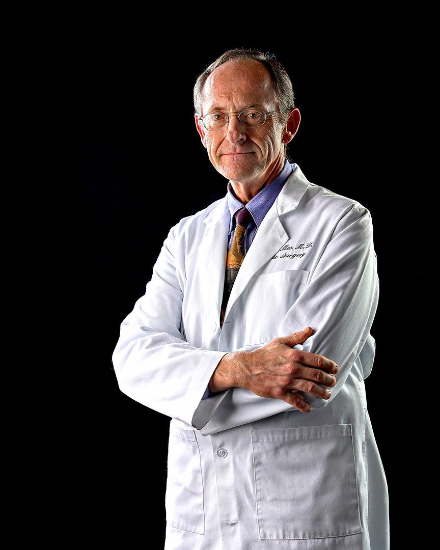 A man in a lab coat and tie is standing with his arms crossed.