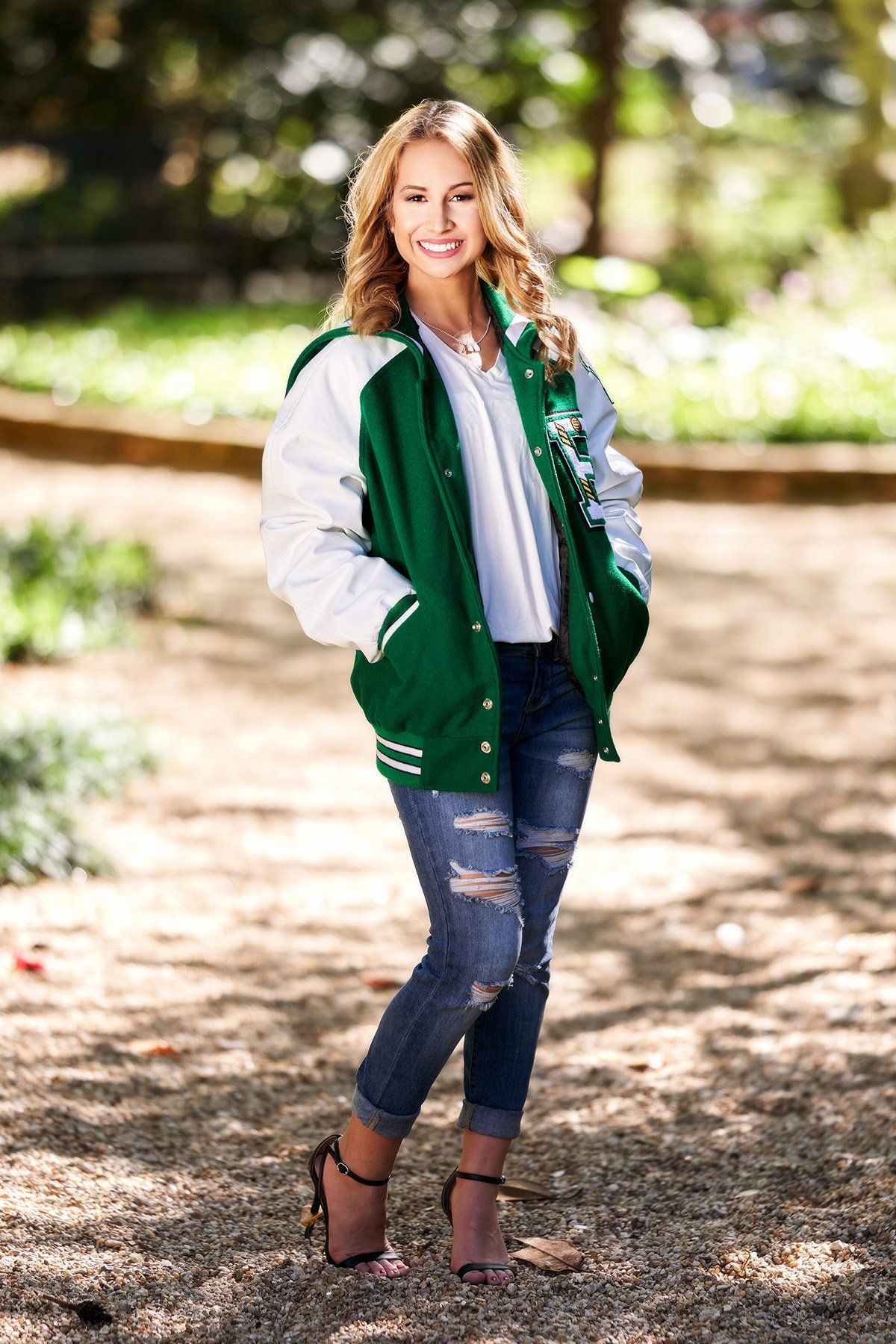 A woman is wearing a green and white varsity jacket and jeans.