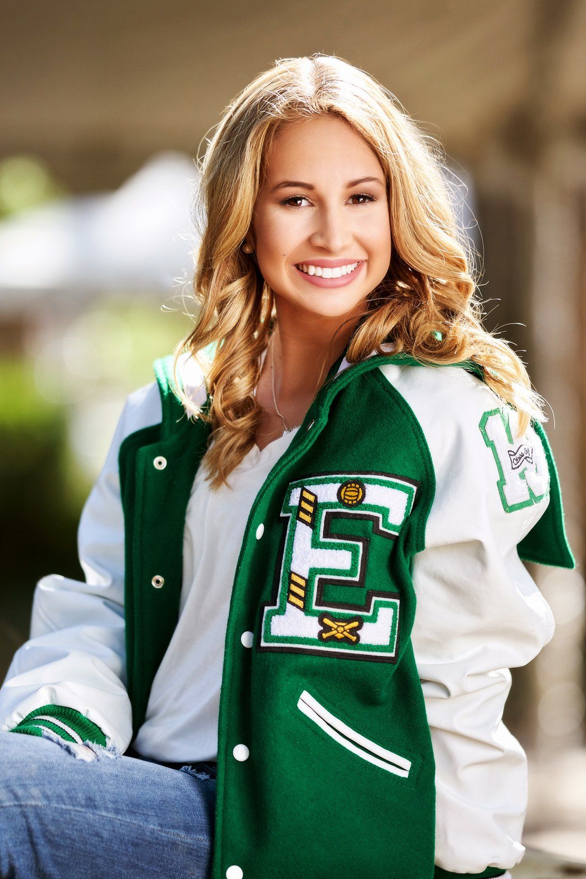 A woman wearing a green and white letterman jacket with the letter e on it.