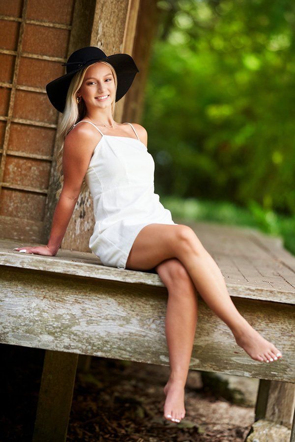 A woman in a white dress and black hat is sitting on a bench.