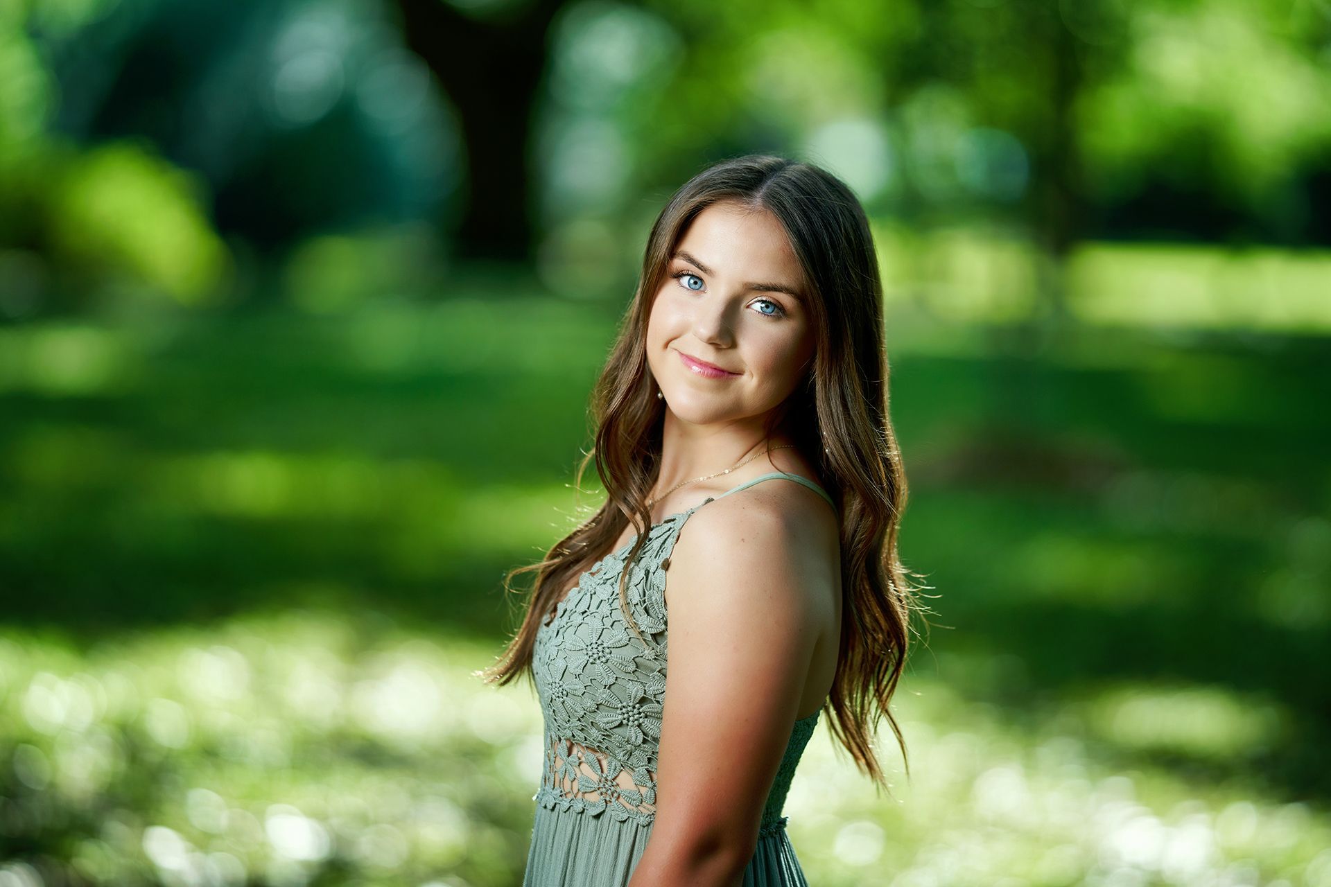 A young woman in a green dress is standing in a park.