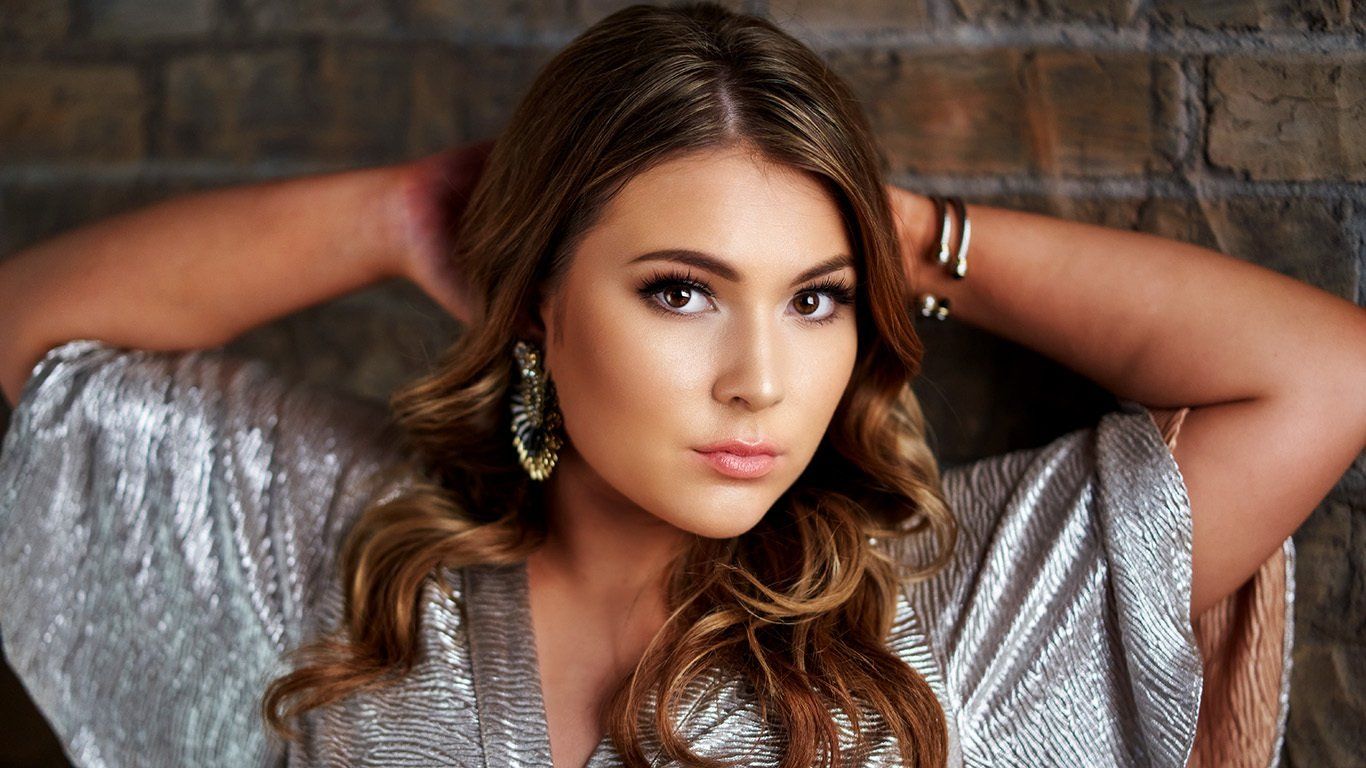 A woman in a silver dress is standing in front of a brick wall.