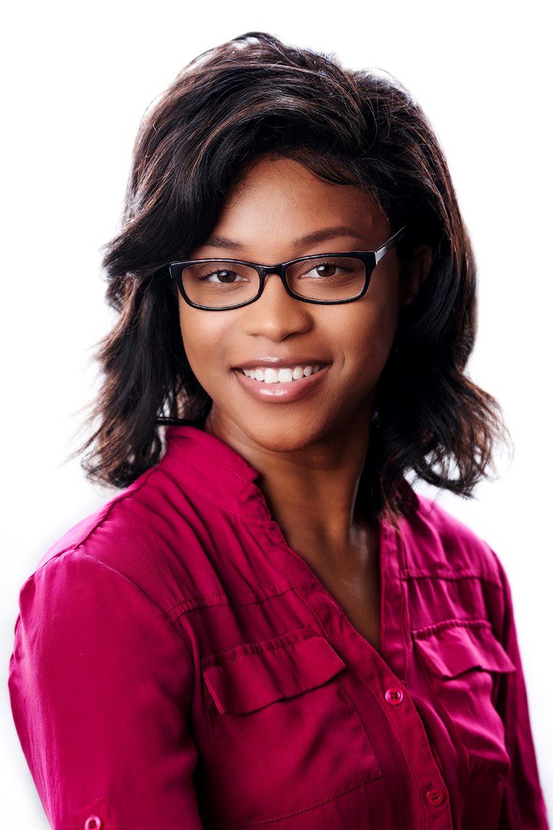 A woman wearing glasses and a pink shirt smiles for the camera