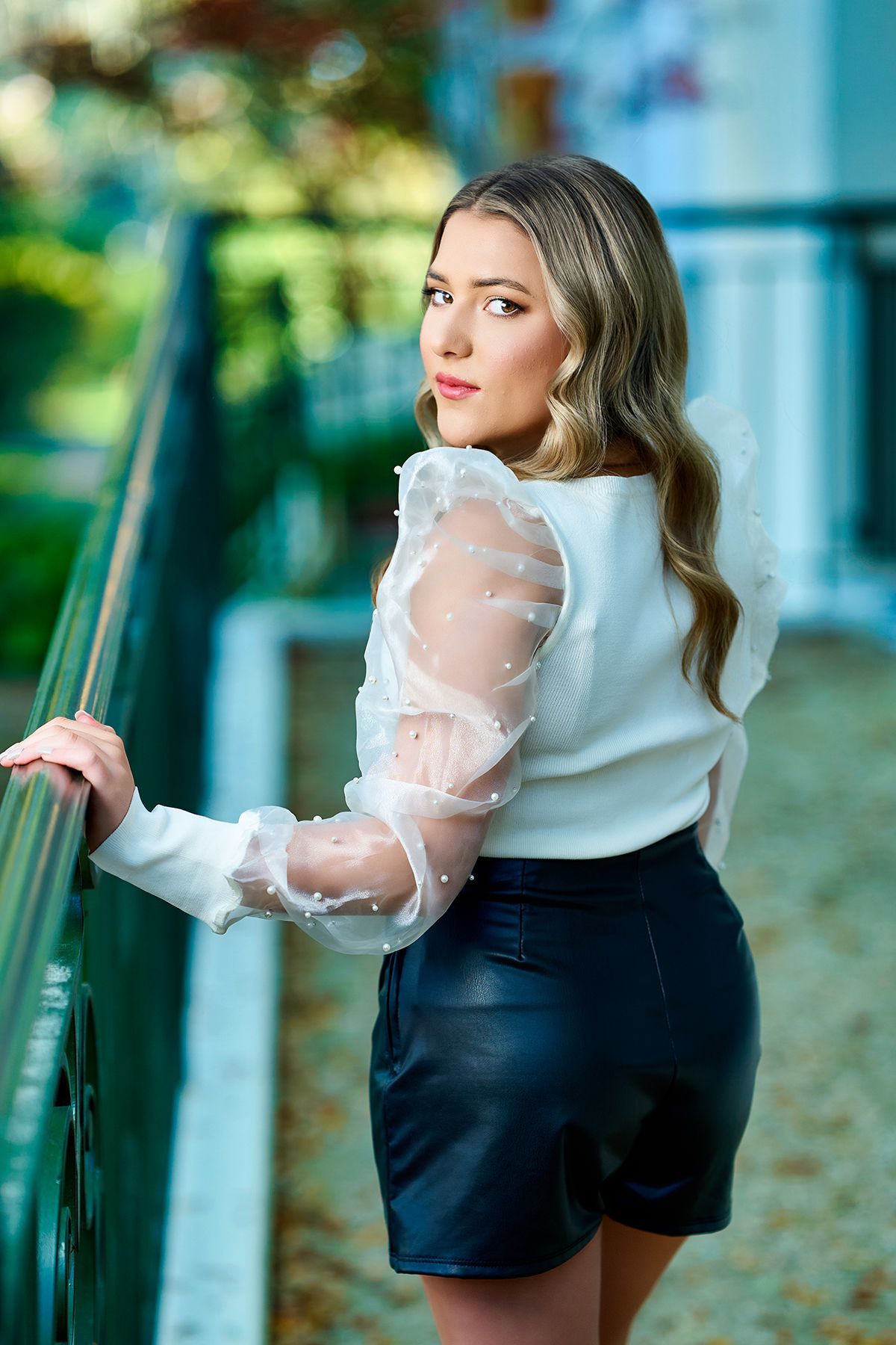 A young woman is sitting on a railing in front of a brick building.