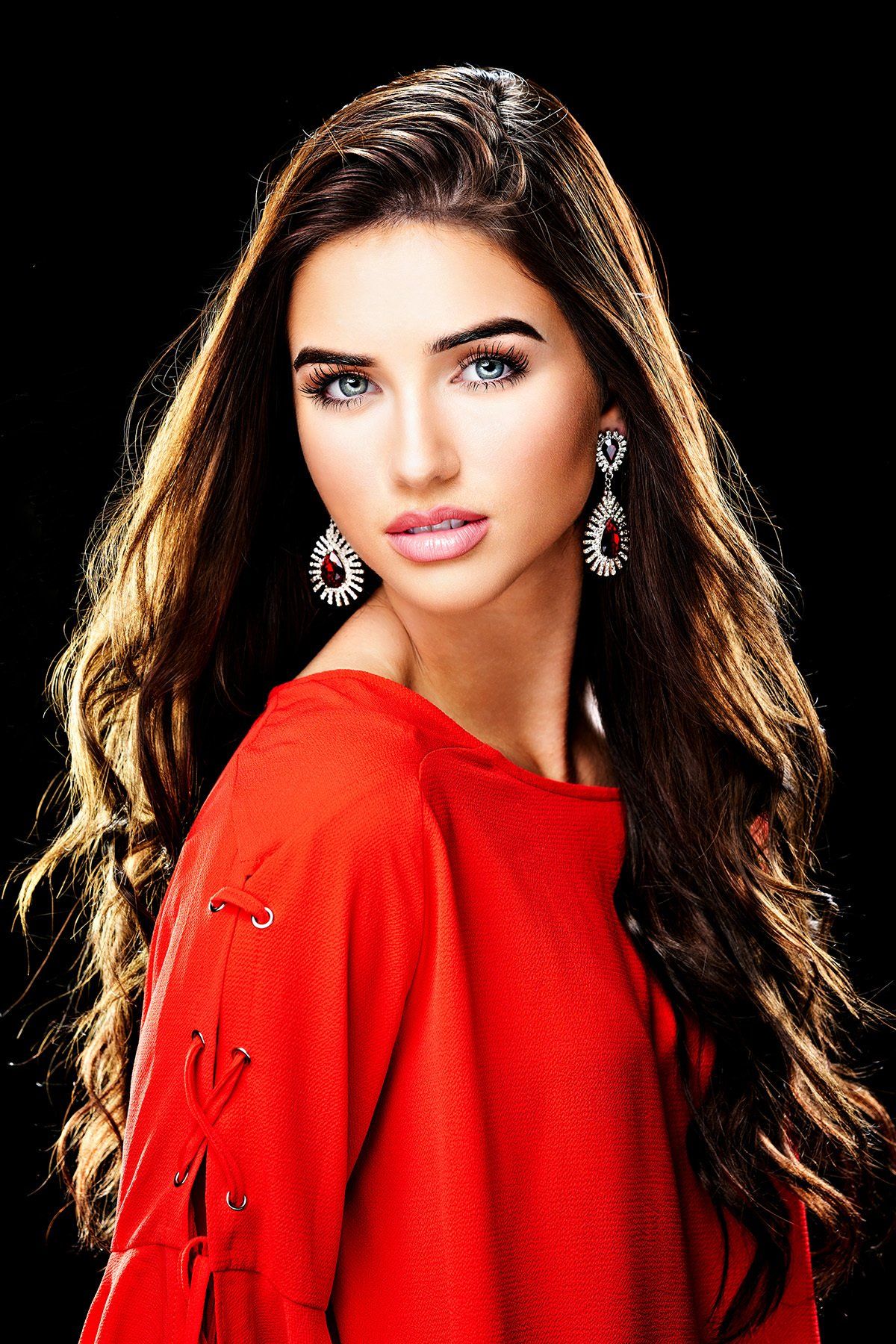 A woman with long hair wearing a red sweater and earrings