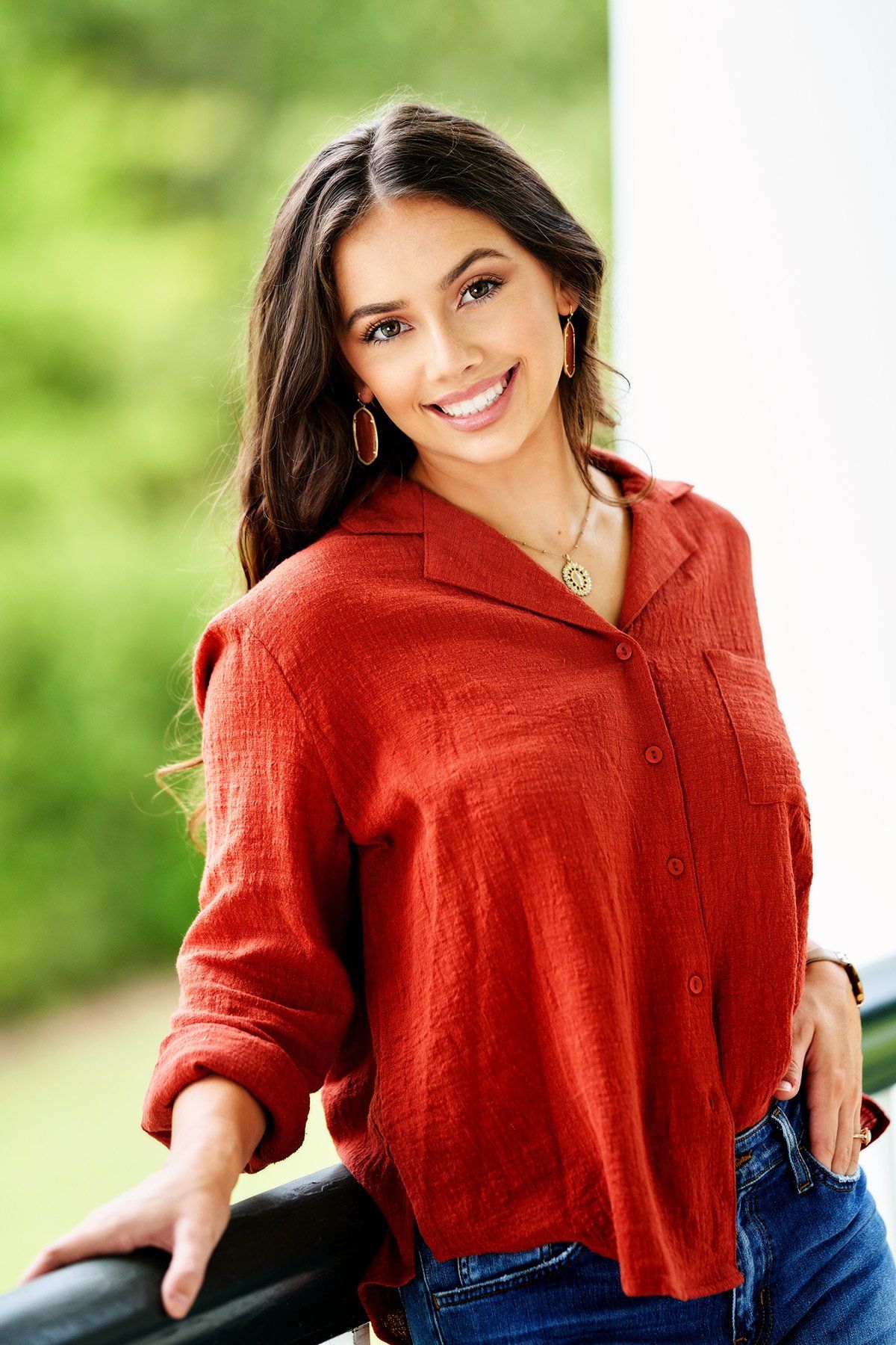 A woman in a red sweater is leaning on a railing and smiling.