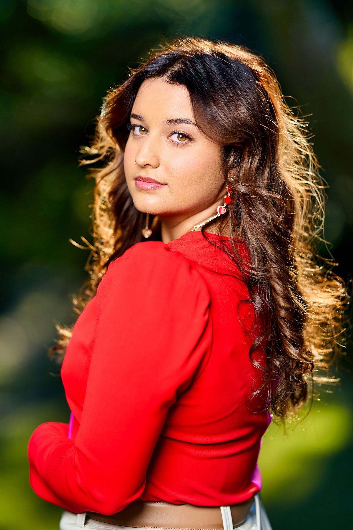 A woman in a red top is standing with her arms crossed.