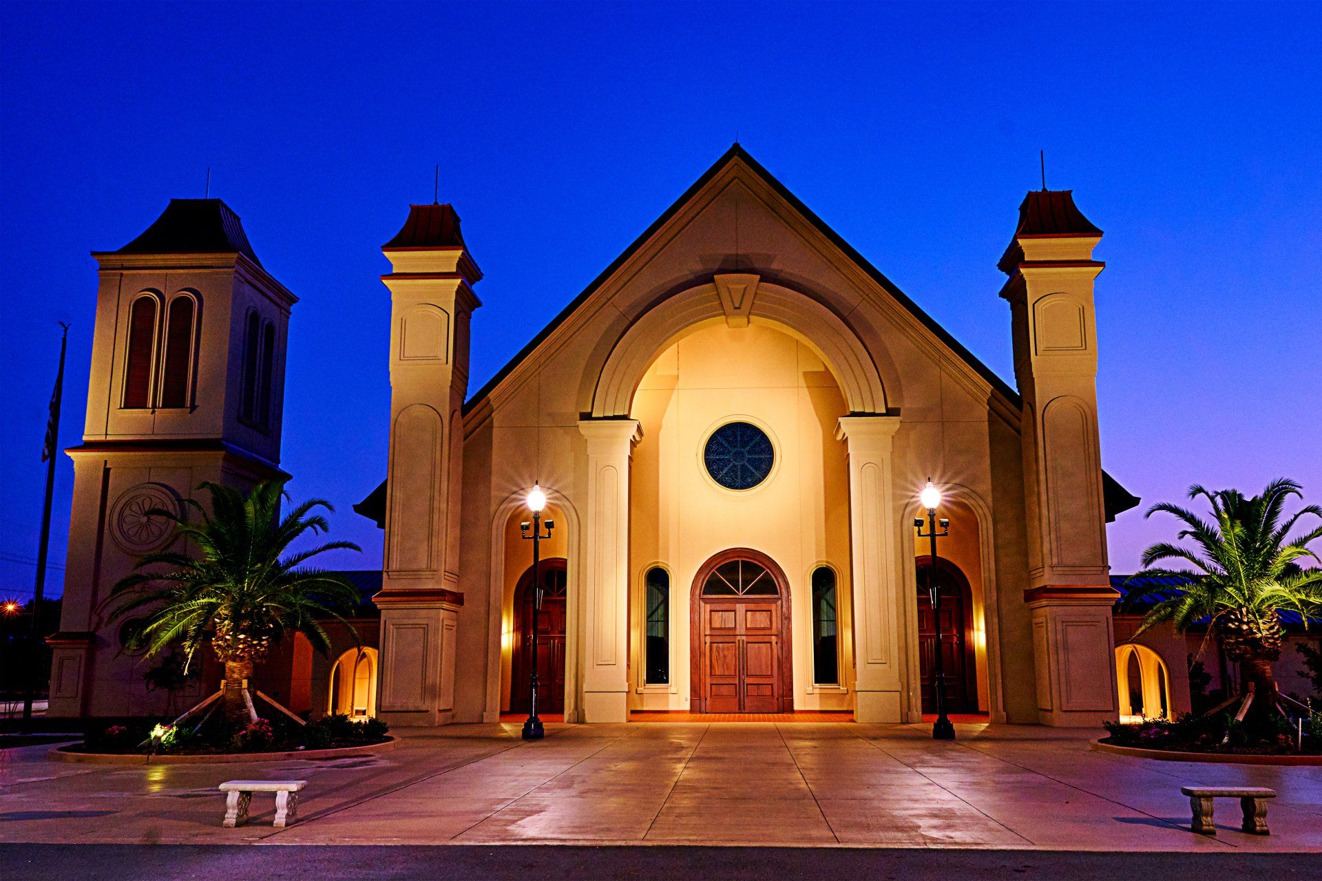 A church is lit up at night with palm trees in front of it