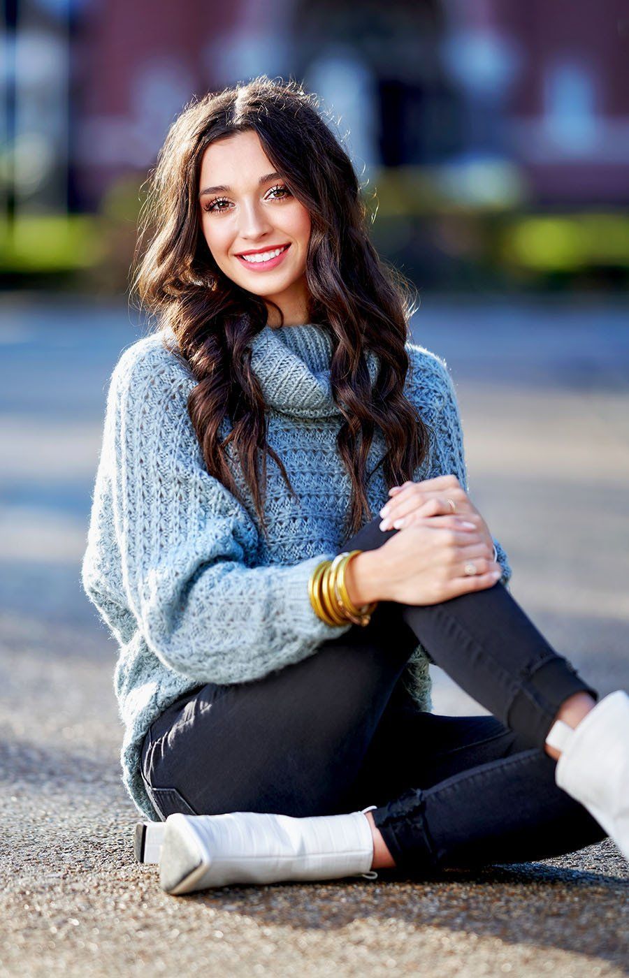 A woman is sitting on the ground wearing a blue sweater and white boots.
