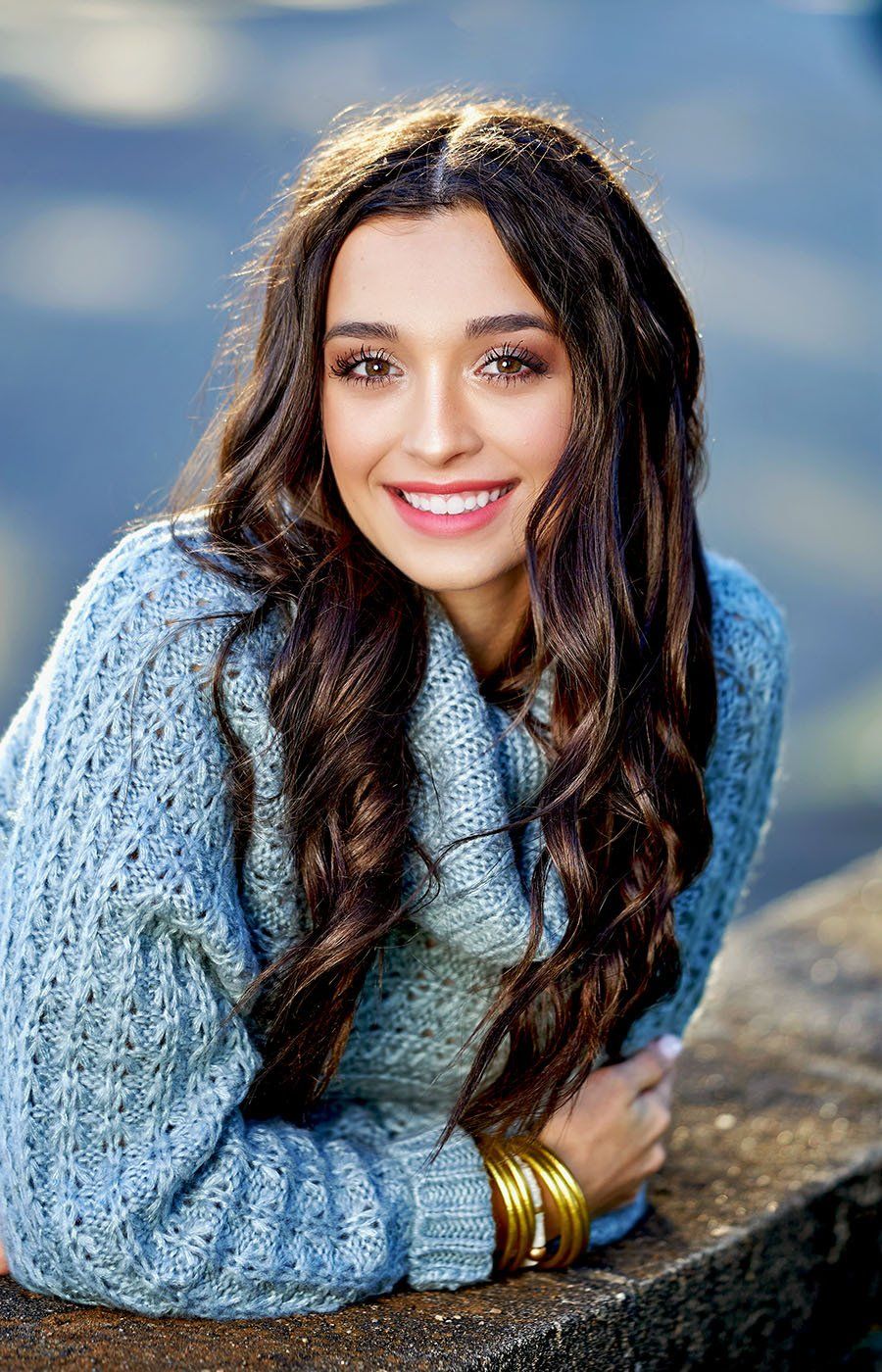 A woman in a blue sweater is laying on a rock and smiling.