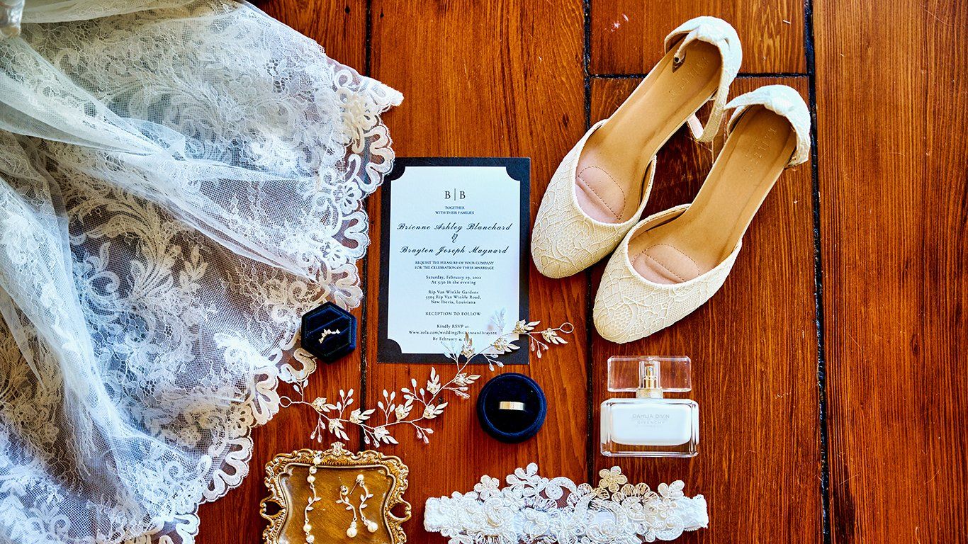 A wedding dress , shoes , perfume , rings , and garter are laid out on a wooden floor.