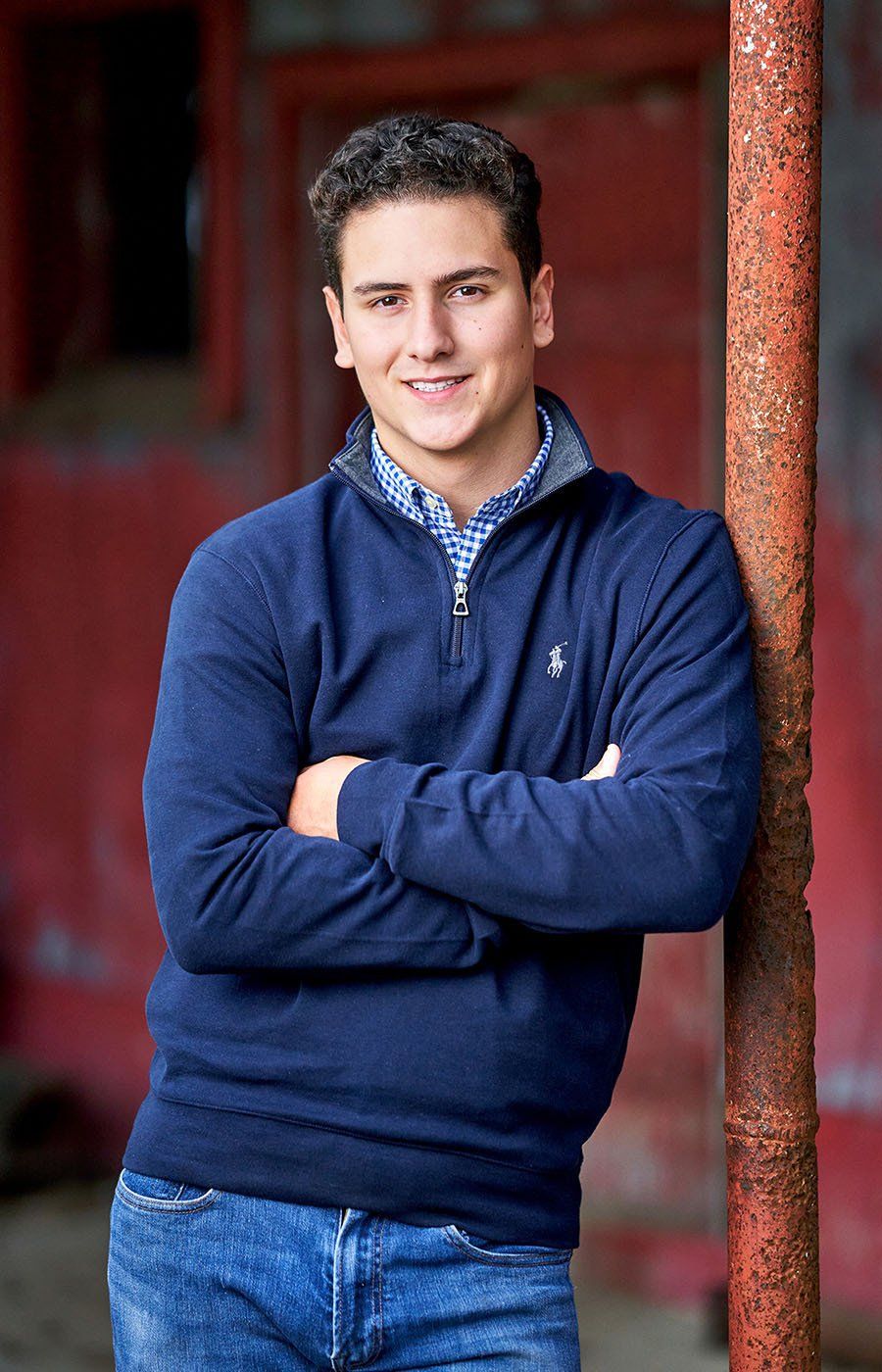 A young man in a blue sweater is leaning against a rusty pole.