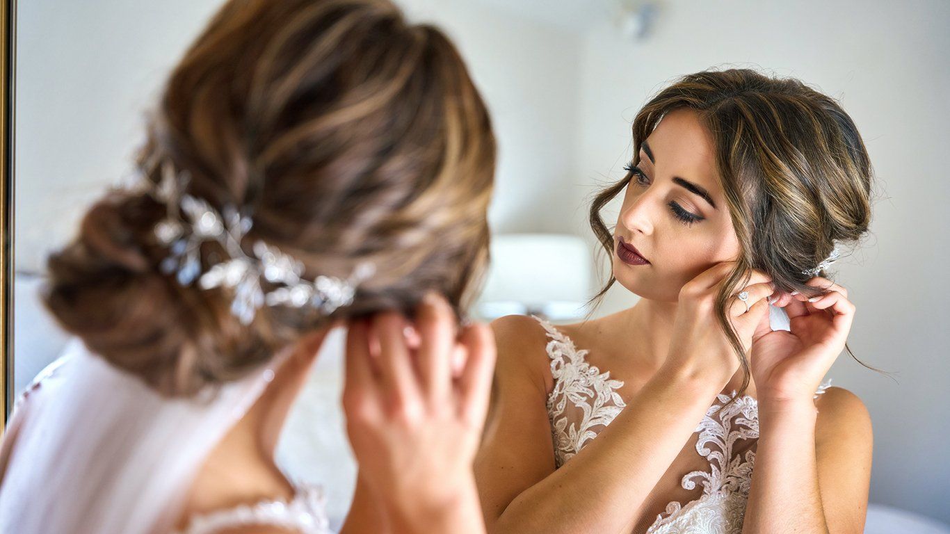 A bride is putting on her earrings in front of a mirror.