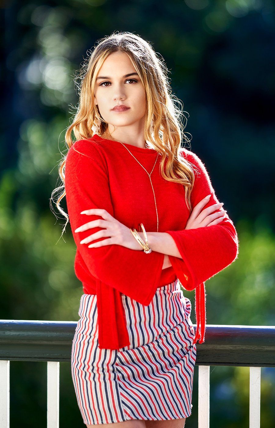 A woman in a red sweater and striped skirt is leaning on a railing.
