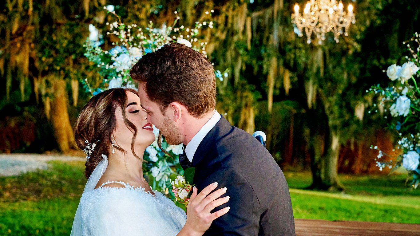 A bride and groom are kissing in front of a chandelier.