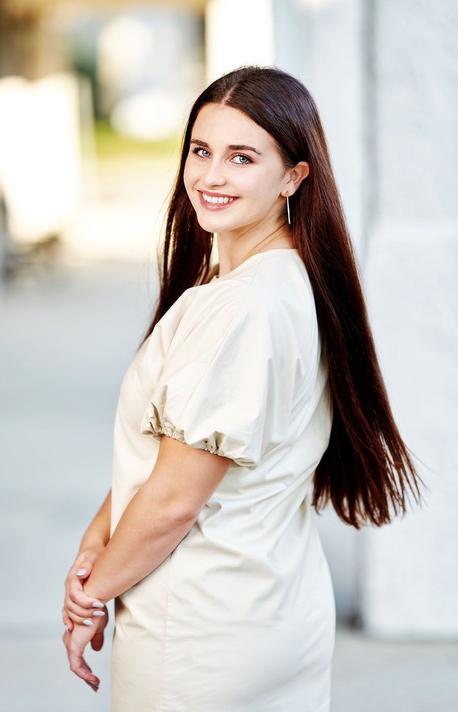 A woman with long hair is wearing a white dress and smiling.