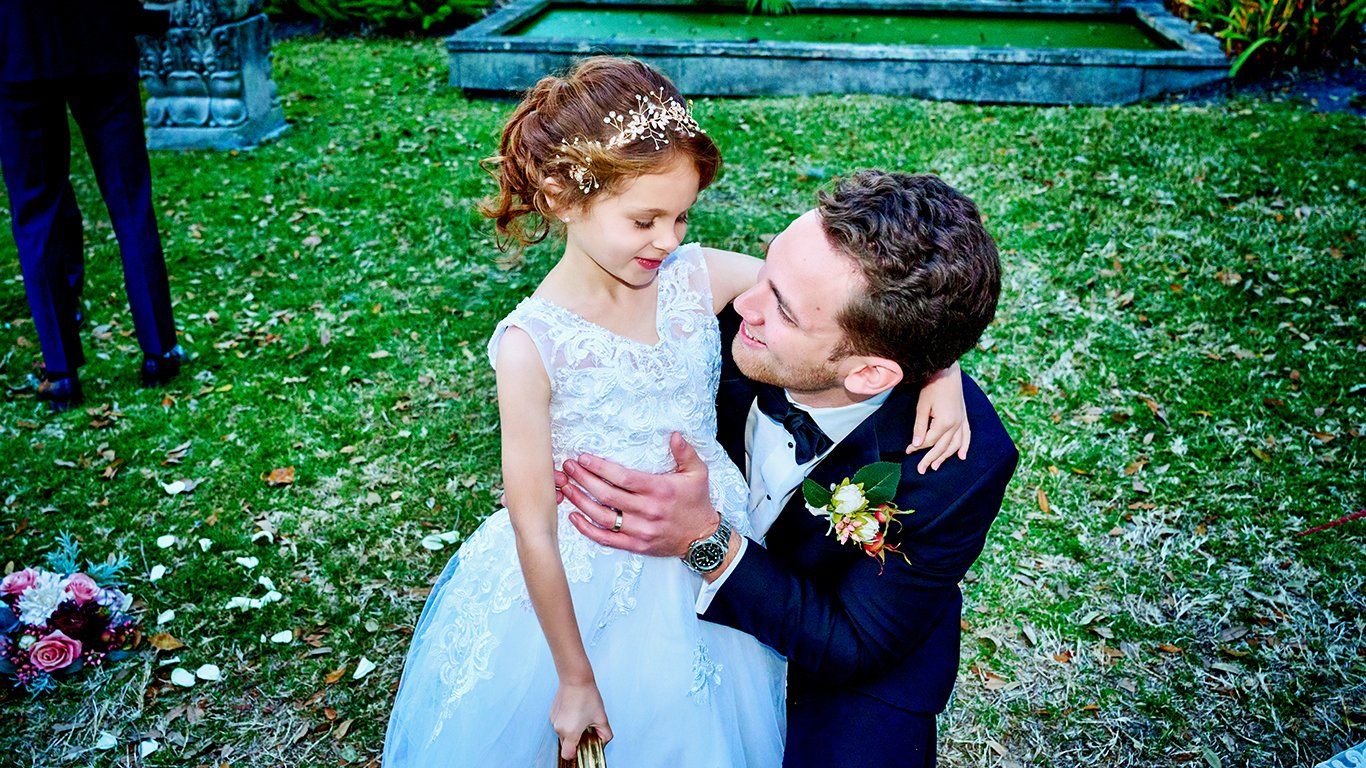 A bride and groom are posing for a picture with a little girl in a flower girl dress.