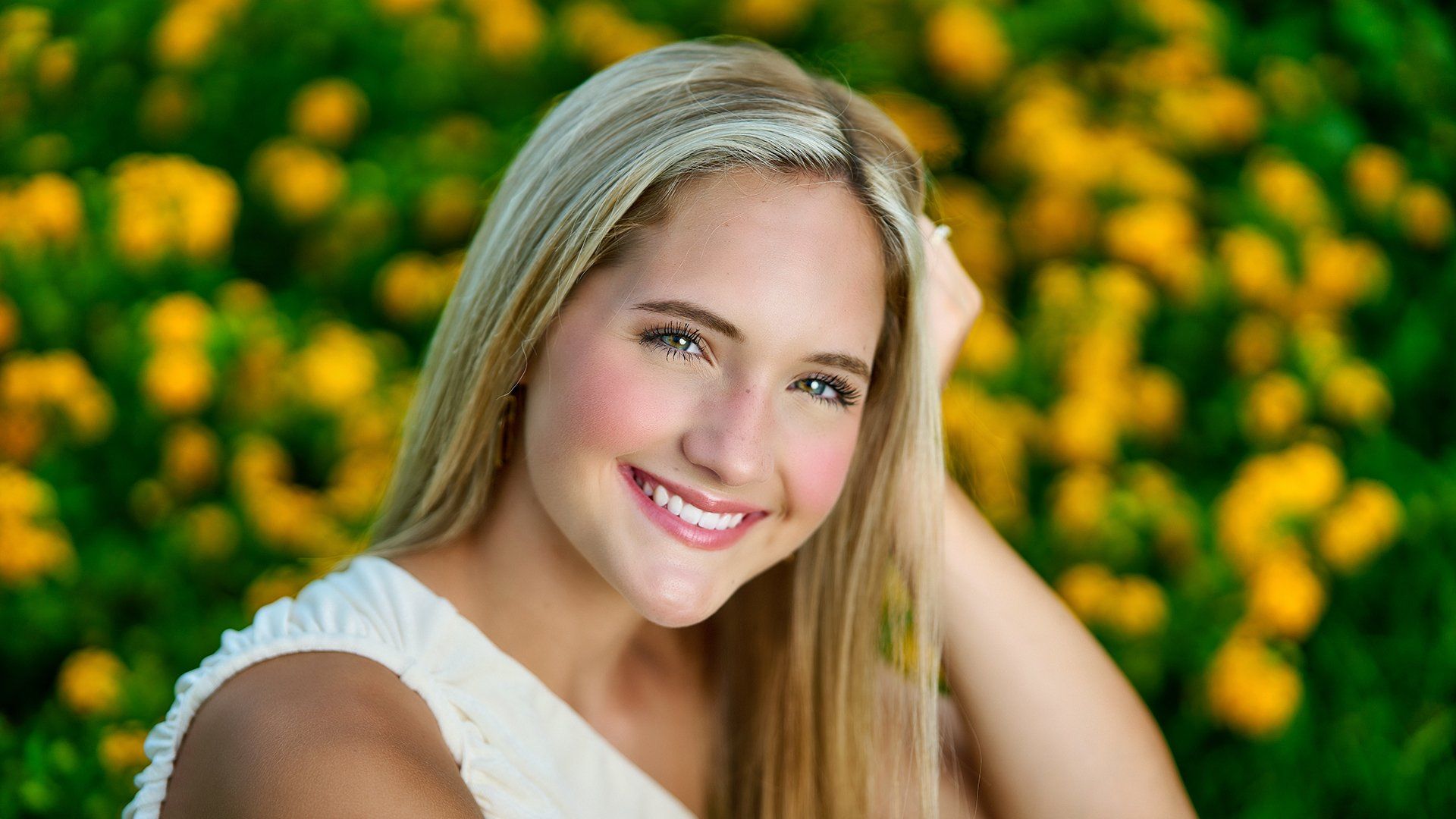A young woman is smiling in front of a field of yellow flowers.