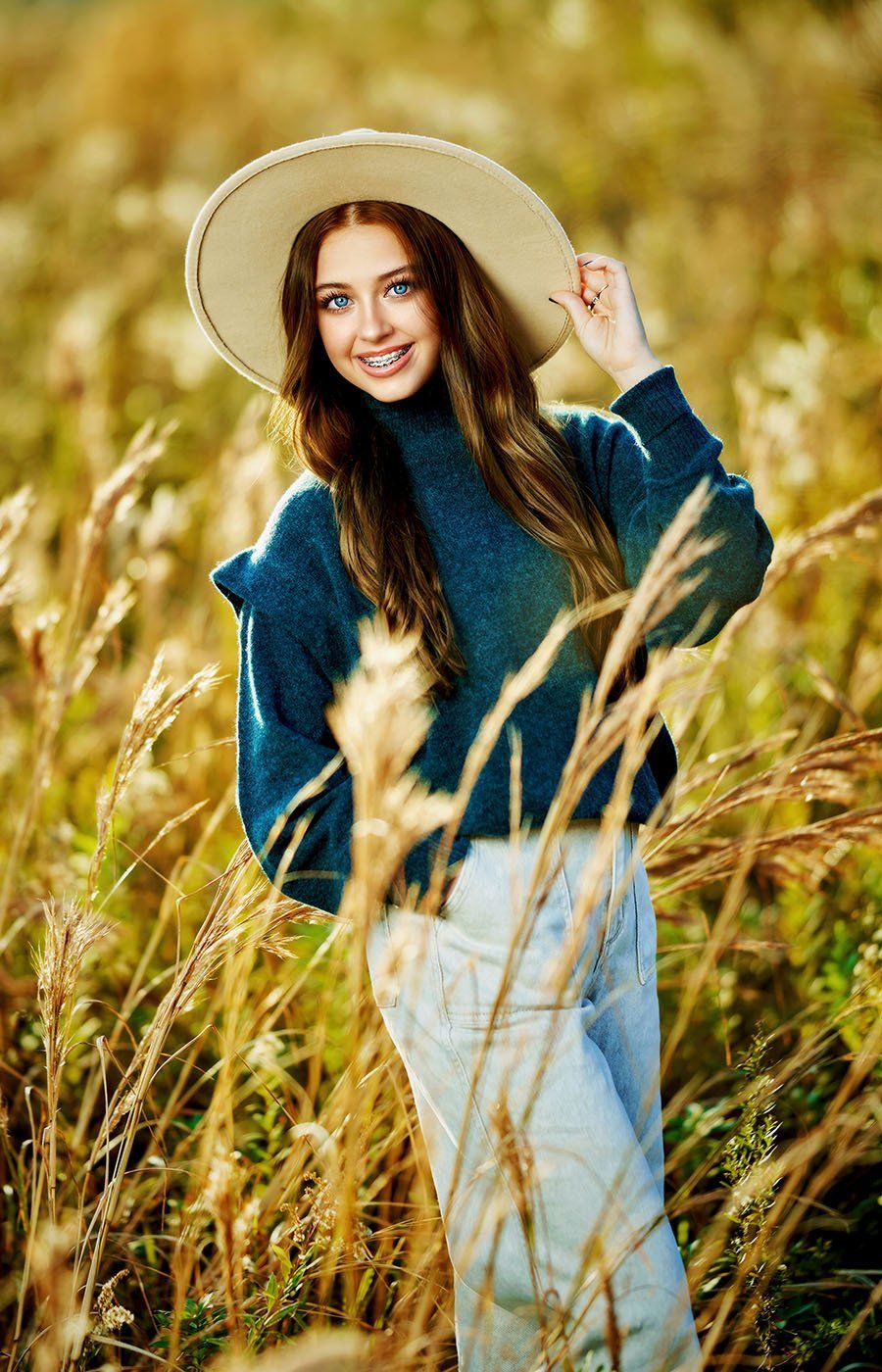 A woman wearing a hat and a sweater is standing in a field of tall grass.