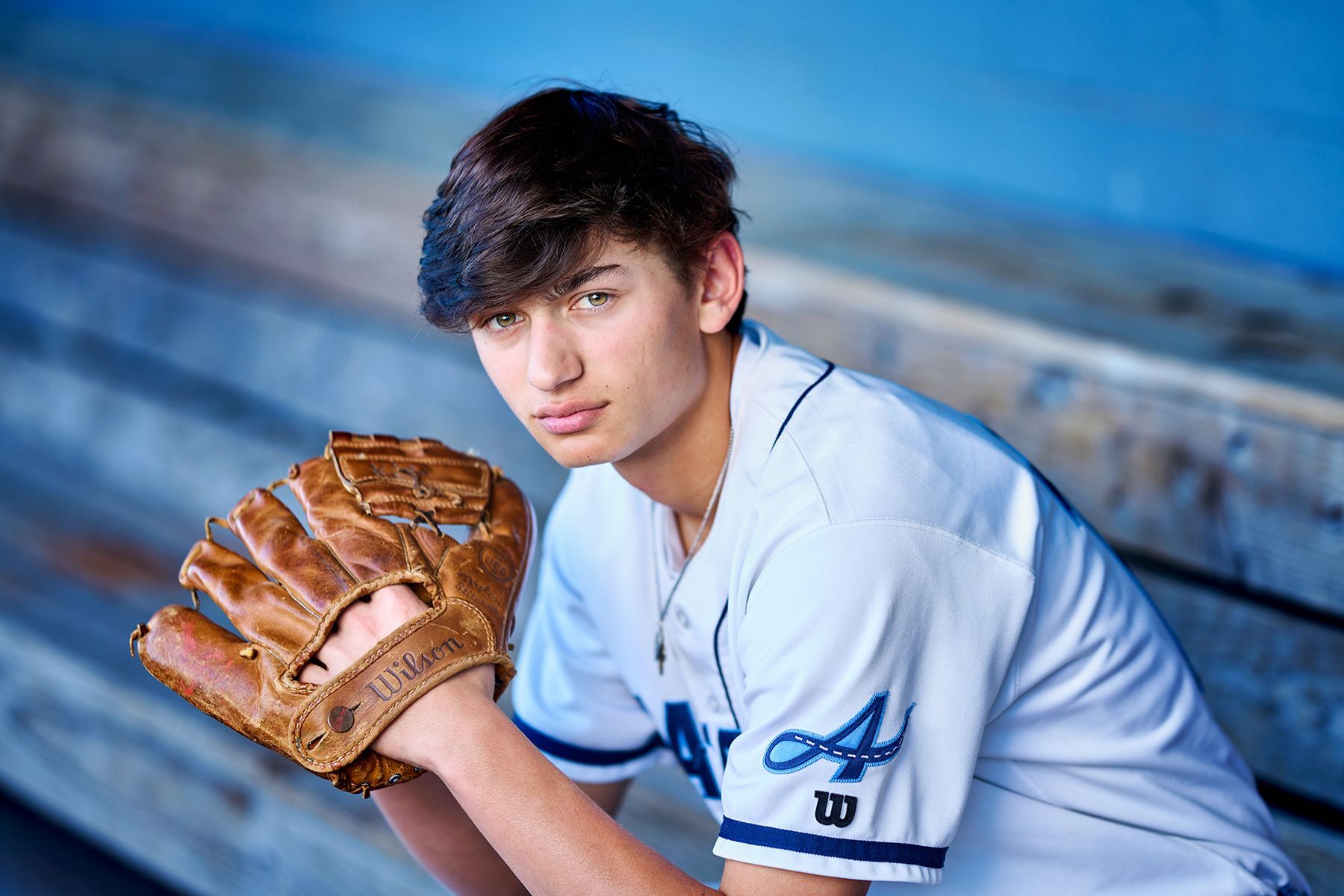 A young man in a baseball uniform is sitting on a bench holding a baseball glove.
