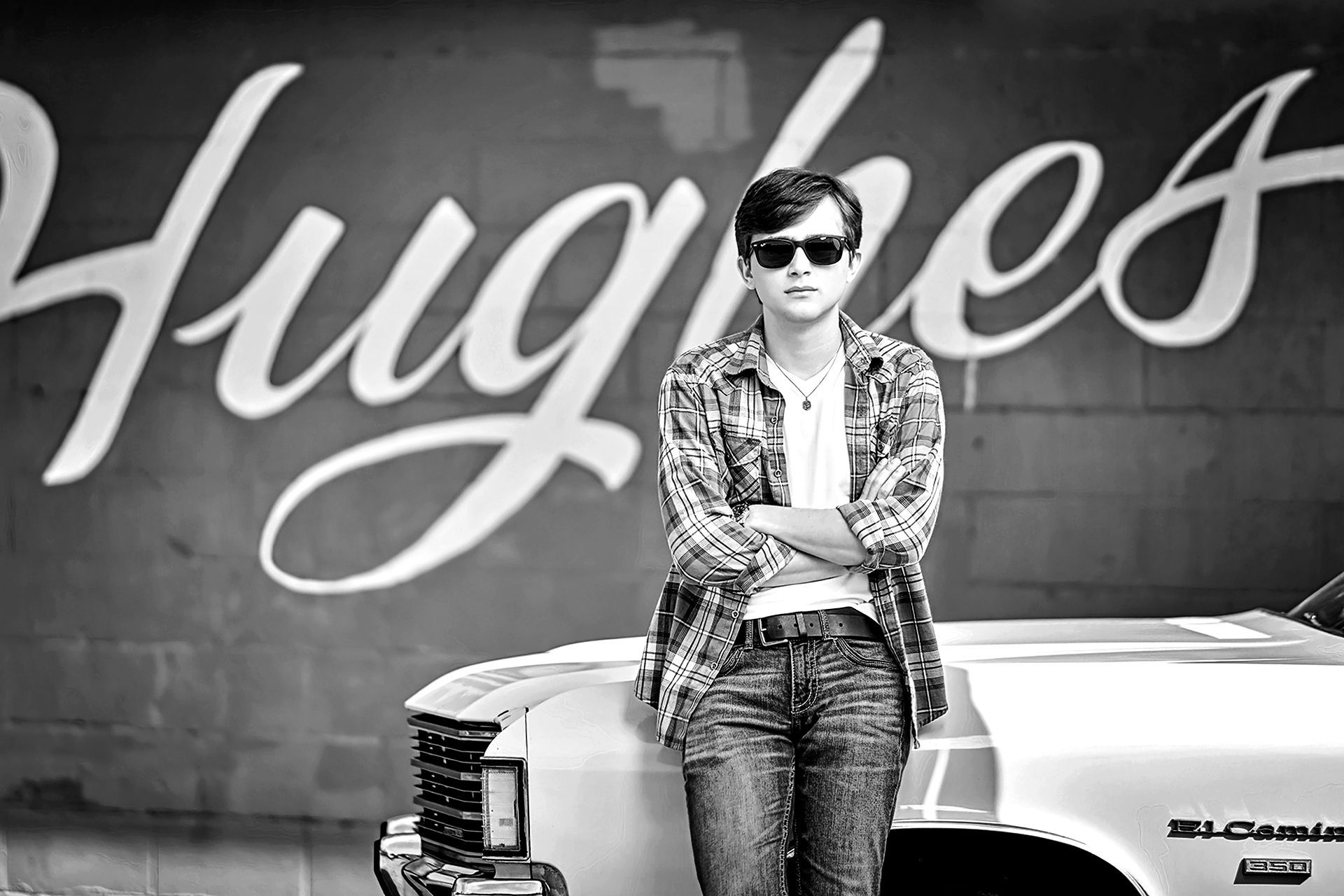 A man standing next to a car in front of a wall that says hughes