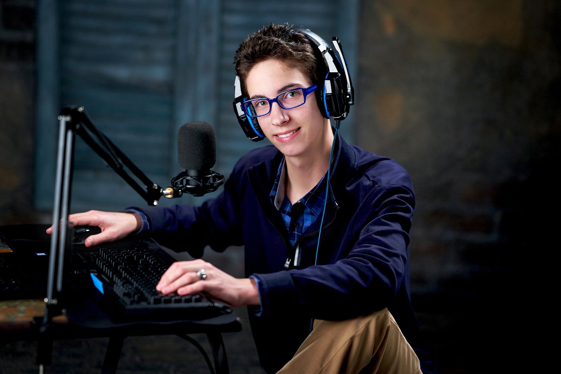 A young man wearing headphones and glasses is sitting in front of a microphone.