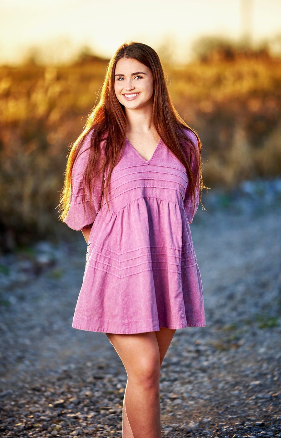 A woman in a purple dress is standing on a dirt road.