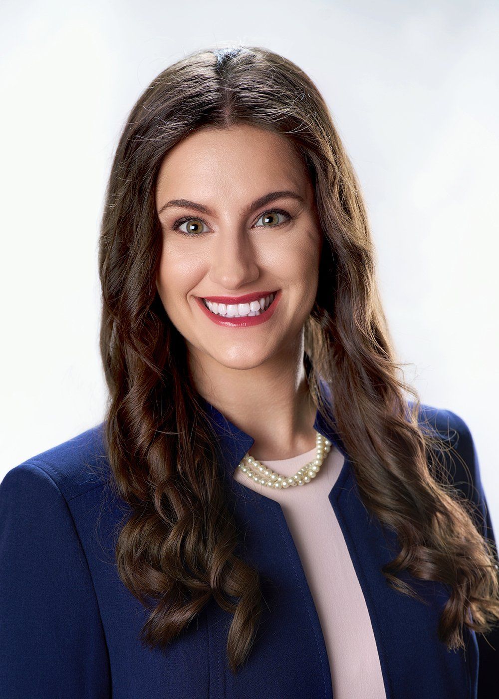 A woman wearing a blue jacket and a pearl necklace is smiling for the camera.