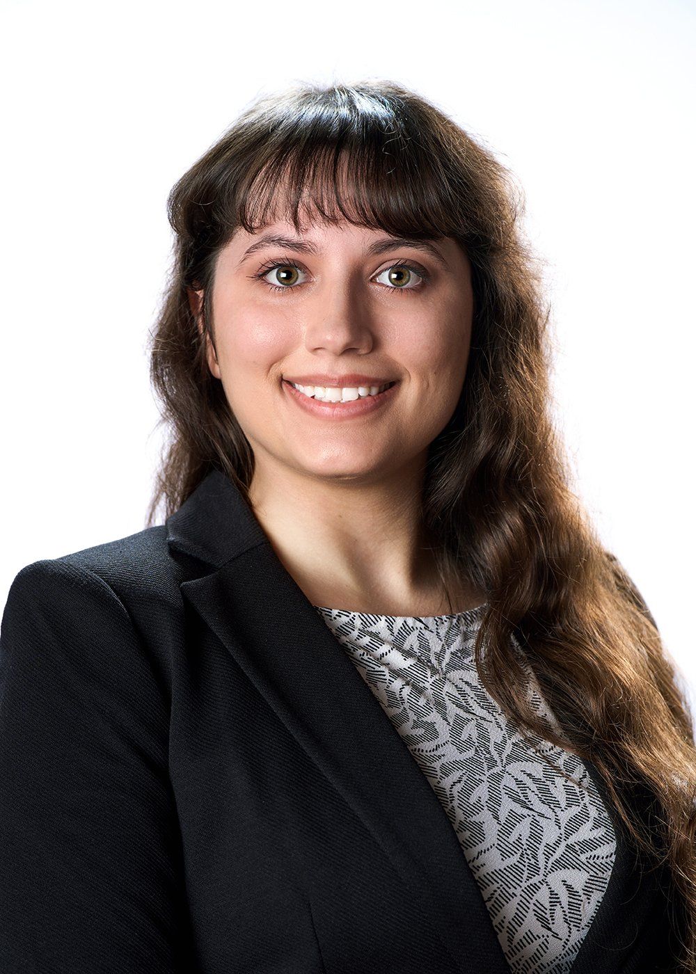 A woman with long hair is wearing a black jacket and smiling.