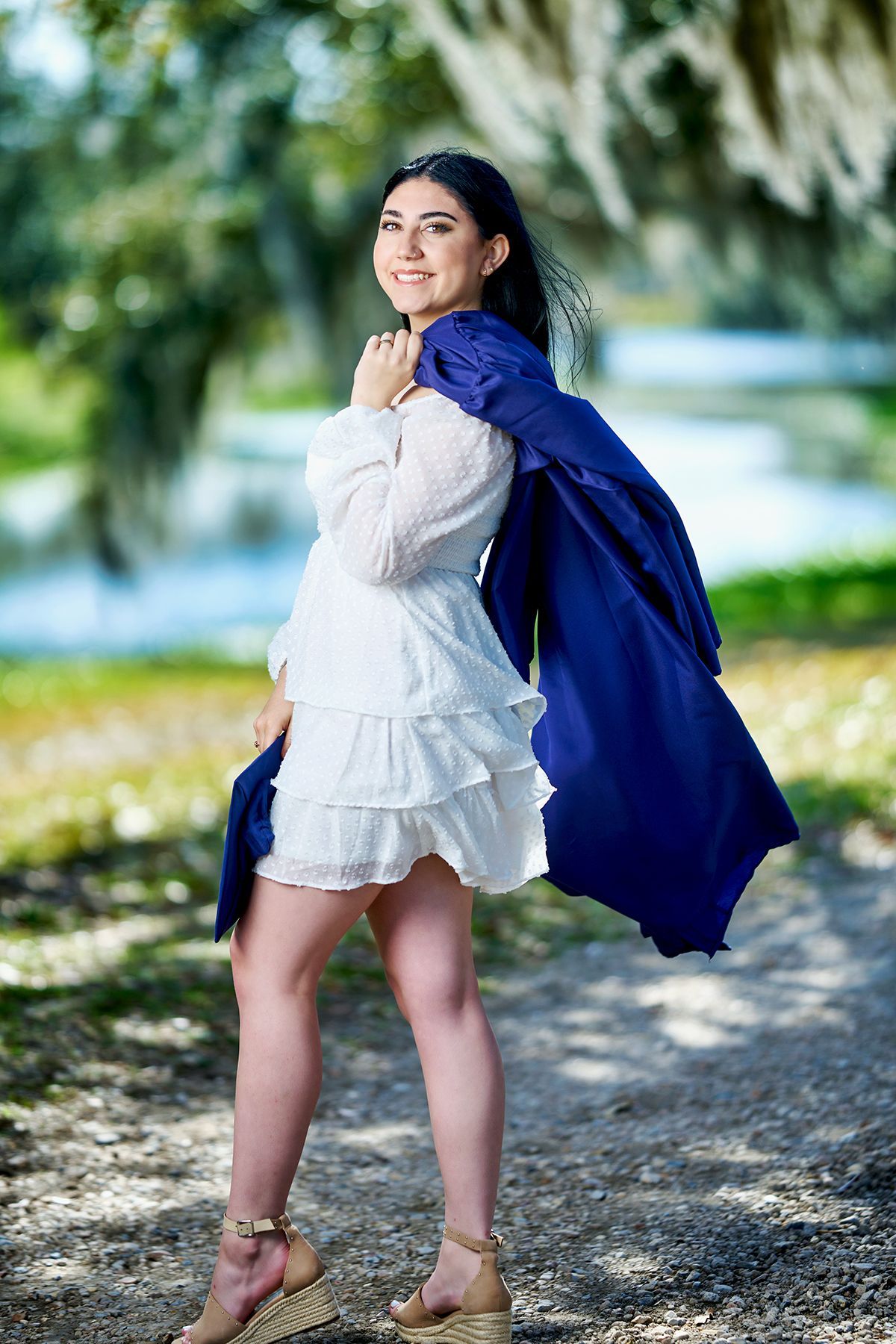 A woman in a white dress is holding a blue cape over her shoulder.