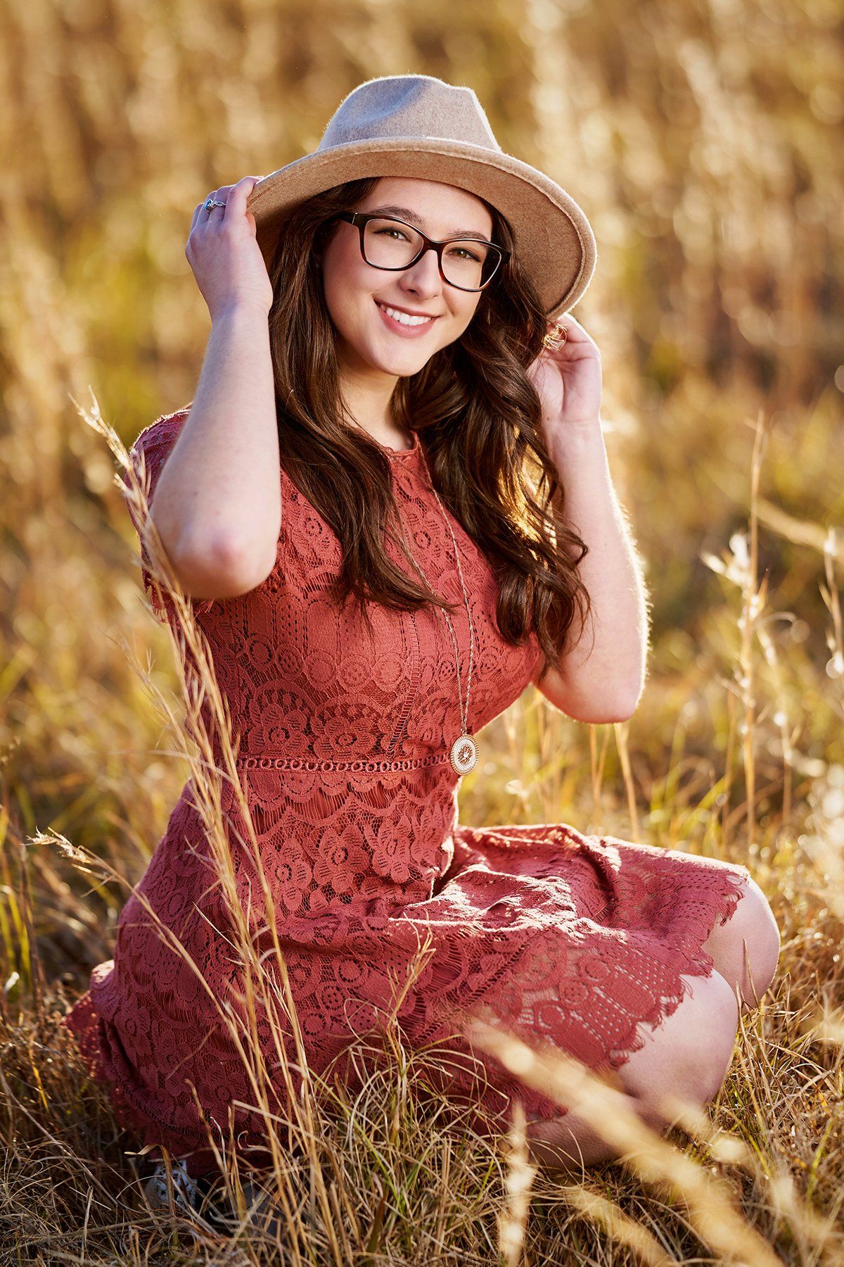 A woman in a red dress and hat is sitting in a field.