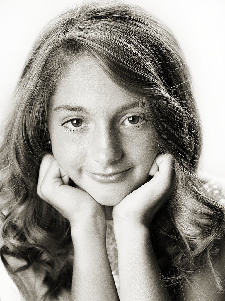A young girl with her hands on her face is smiling in a black and white photo.