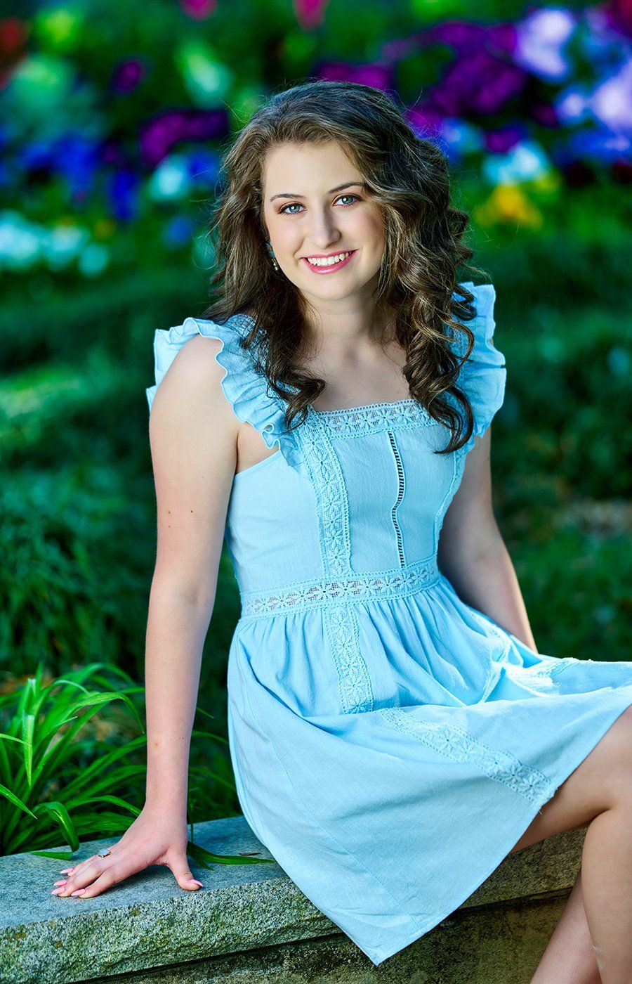 A young woman in a blue dress is sitting on a stone wall.
