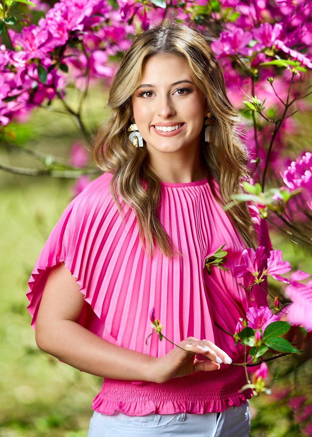 A woman in a pink top is standing in front of a tree with purple flowers.