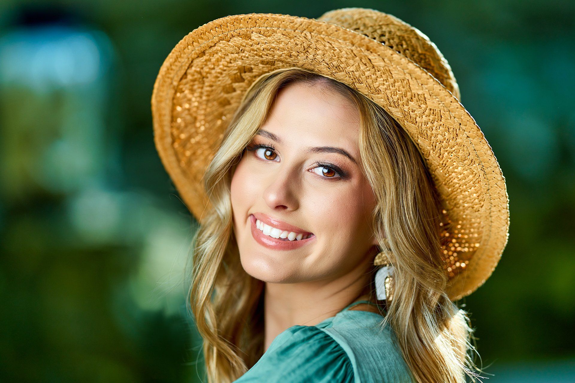 A woman wearing a straw hat and earrings is smiling for the camera.