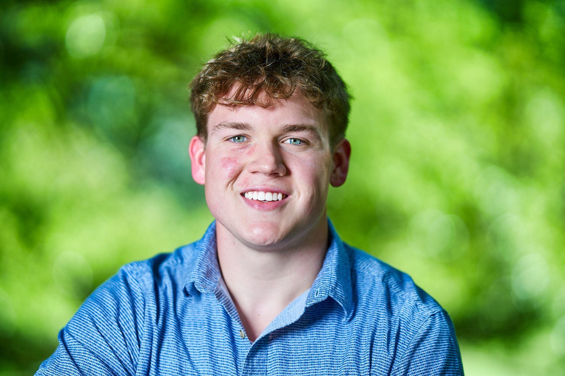 A young man in a blue shirt is smiling for the camera.