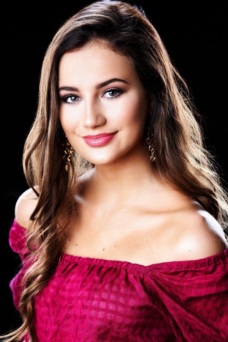 The woman is wearing a red off the shoulder top and earrings.