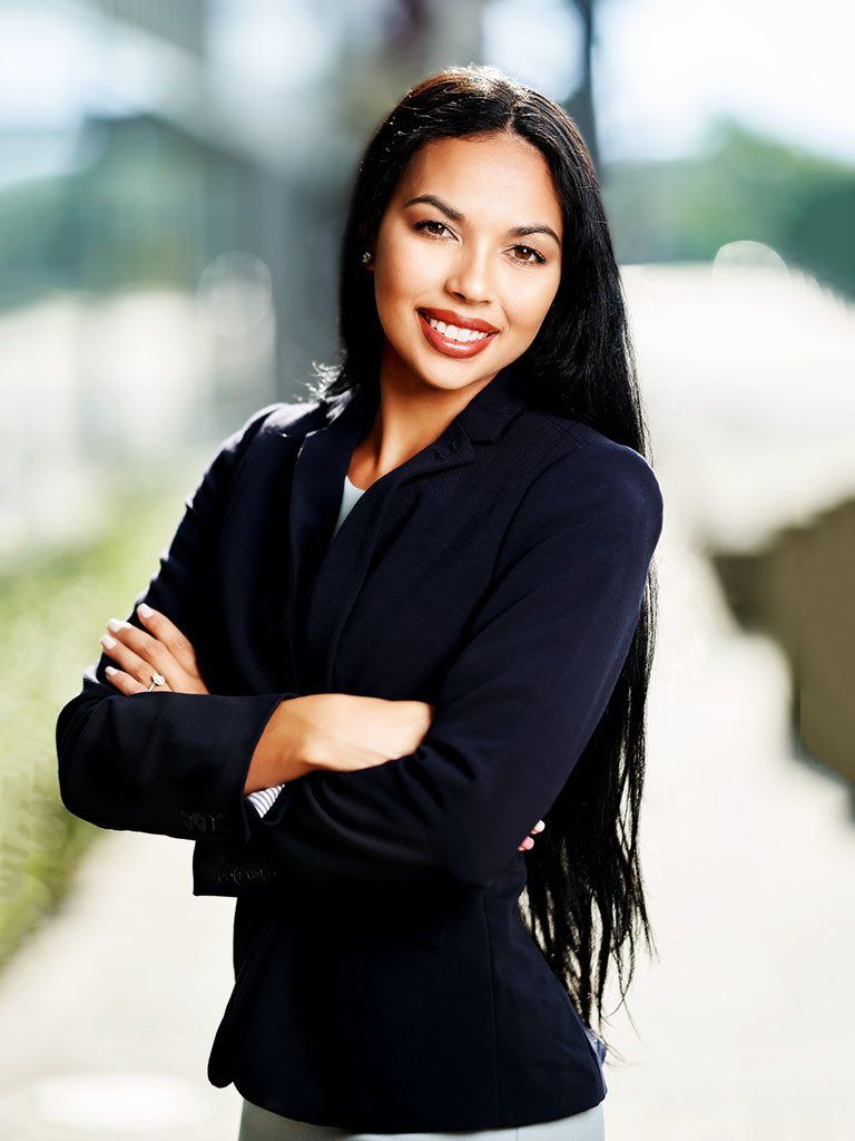A woman in a business suit is standing with her arms crossed and smiling.
