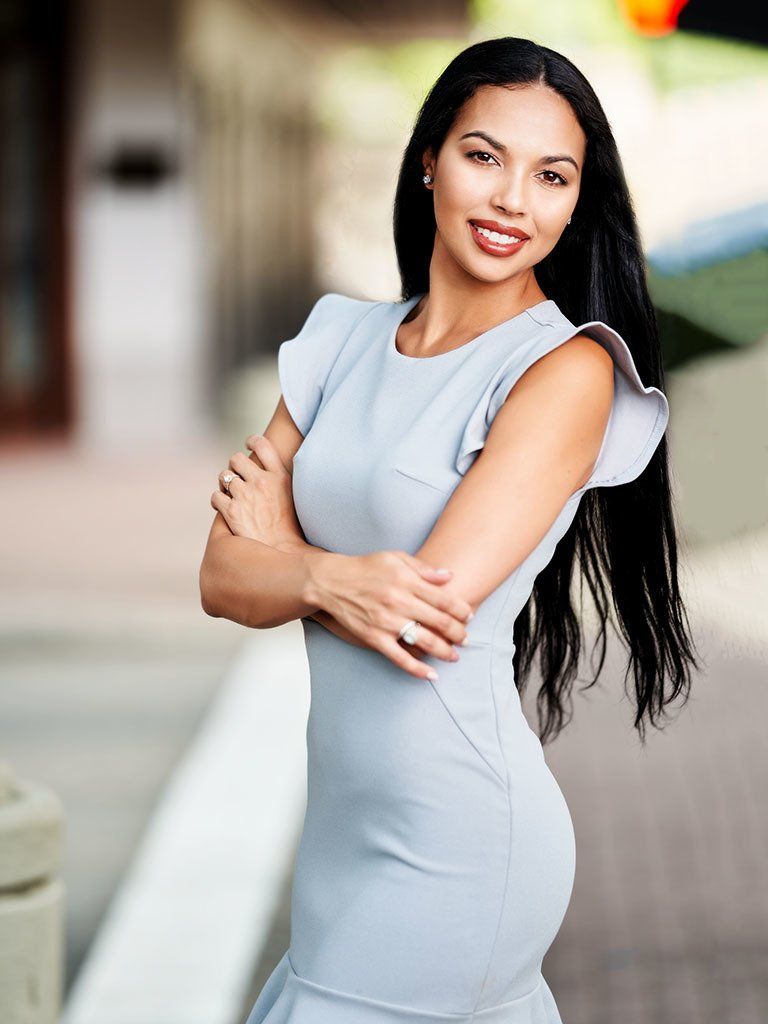 A woman in a light blue dress is standing with her arms crossed.