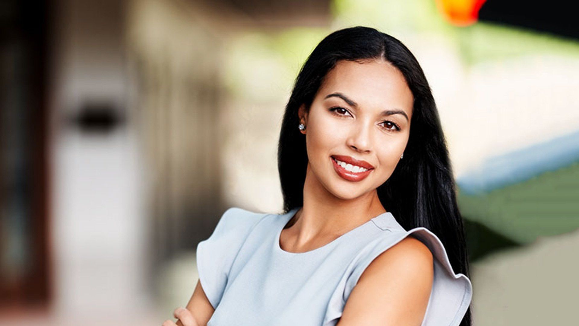 A woman in a blue dress is standing with her arms crossed and smiling.